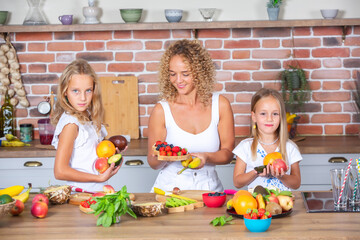 Mother and daughters cooking together in the kitchen. Healthy food concept. Portrait of happy family with fresh smoothies. Happy sisters.