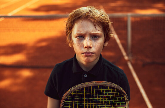 Portrait of a young Caucasian boy posing on a tennis clay court