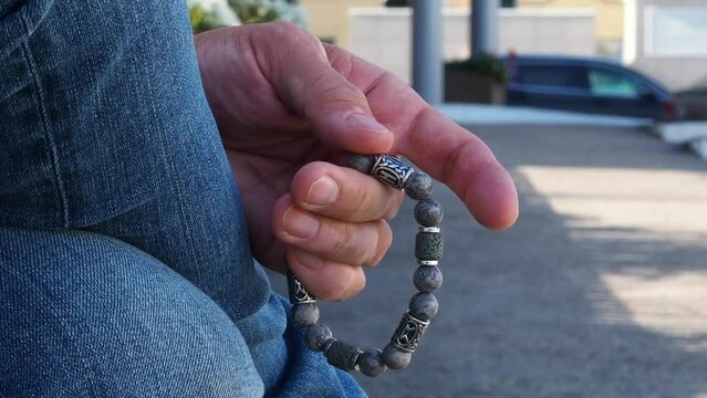 Rosary in hand. Vitiligo disease on the hands. Touch the bracelet with your fingers. Men's accessory made of natural stone. The hand of a man with a stone rosary passes through the rosary.
