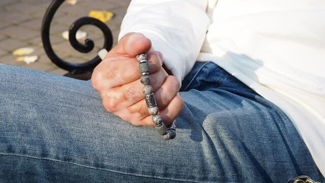 Rosary in hand. Vitiligo disease on the hands. Touch the bracelet with your fingers. Men's accessory made of natural stone. The hand of a man with a stone rosary passes through the rosary.