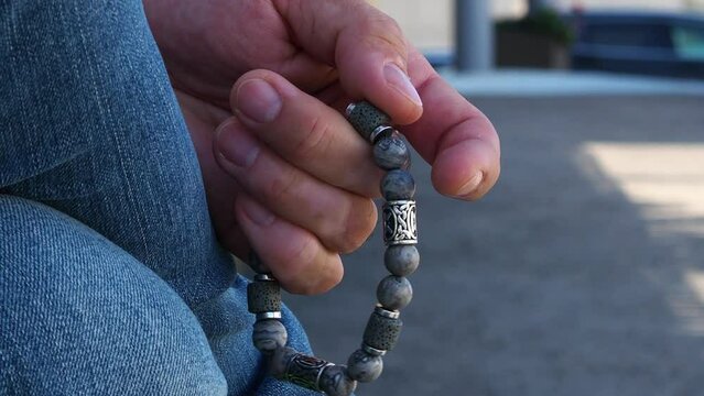 Rosary in hand. Vitiligo disease on the hands. Touch the bracelet with your fingers. Men's accessory made of natural stone. The hand of a man with a stone rosary passes through the rosary.