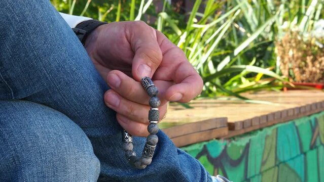 Rosary in hand. Vitiligo disease on the hands. Touch the bracelet with your fingers. Men's accessory made of natural stone. The hand of a man with a stone rosary passes through the rosary.
