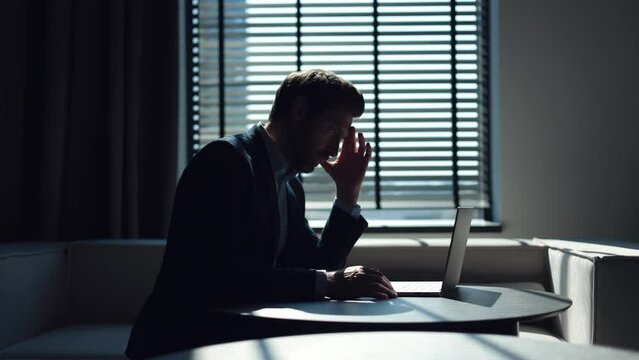 Caucasian entrepreneur feeling despair after receiving email on laptop from bank refusing loan for company. Hopeless man in formal suit sitting at round office desktop, closing eyes and touching head.