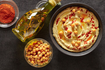 Hummus with olive oil and spices in bowl, on slate stone plate round, dark background, top view.