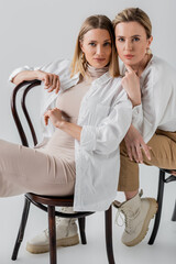 Obraz premium stylish elegant blonde sisters sitting on chairs in fashionable pastel attire, fashion concept