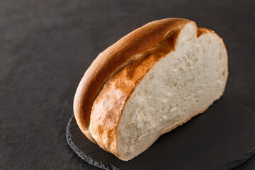 Light round loaf bread cut half, side view, on dark background, selective focus