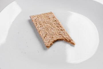 A bitten slice of buckwheat crispbread on a white plate with crumbs