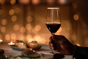 Close up of male hand holding wine glass at dinner table with Christmas lights in background, copy space