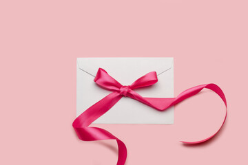 Un sobre blanco cerrado con un lazo rosa sobre un fondo rosa pastel. Vista superior y de cerca. Copy space