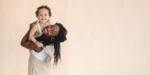 African-American mother with baby smiles and rejoices on beige background Minimalist portraits, space for text