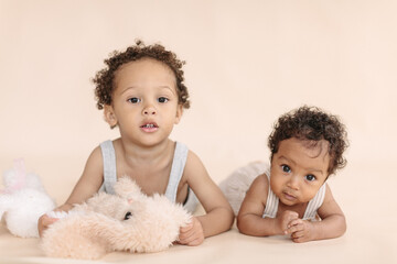 African-American children, a baby girl and a 4-year-old boy looking at the camera on a beige...