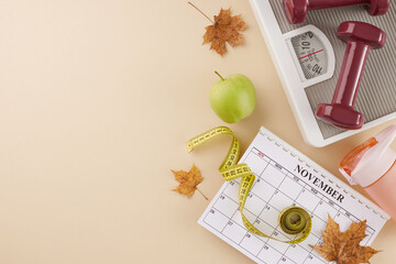 Evolving your body in autumn. Top view shot of calendar, weight scale, tape measure, dumbbells, fresh apple, water bottle, dry autumn leaves on beige background with advert space
