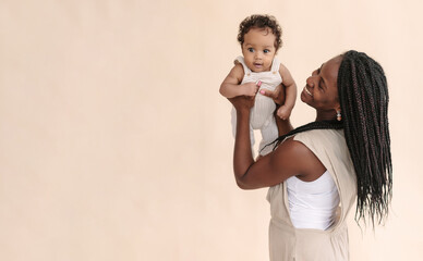 African-American mother with baby smiles and rejoices on beige background Minimalist portraits, space for text