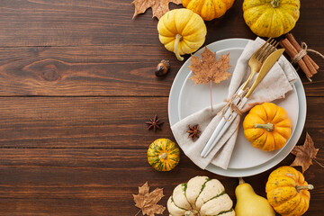 Fototapeta na wymiar Highlight the blessings of autumn in your table arrangement. Top view of plates, cutlery, ripe pumpkins, fallen leaves, anise, cinnamon sticks, acorns on wooden background with promo zone
