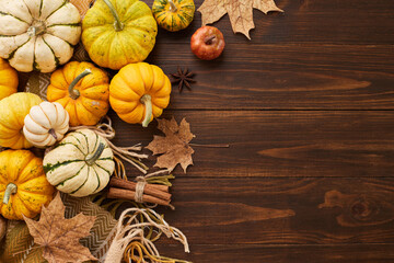 Celebrate the autumn harvest scene. Top view photo of cozy plaid, orange pumpkins, cinnamon sticks, fallen autumn leaves, anise on wooden background with promo area