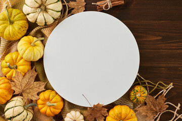 Embracing the autumn harvest. Top view flat lay of pumpkins, cozy blanket, maple leaves on wooden background with blank circle for promo or text