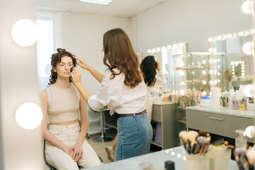 Reflection on mirror of unrecognizable female make-up artist applying cosmetic tonal foundation for...