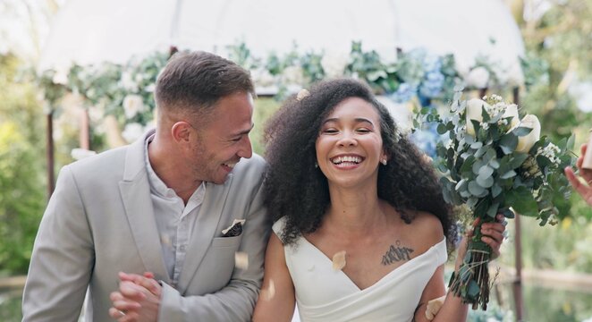 Couple, wedding and celebration with flower confetti for event, walk and outdoor in nature. Girl, happy interracial marriage and floral bouquet in park, holding hands or applause from crowd in aisle - Powered by Adobe