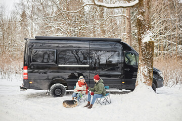 Wide angle portrait of young couple travelling by van outdoors in winter forest with cute dog, copy...