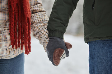 Close up of young couple holding hands in winter wearing cute knit mittens, copy space