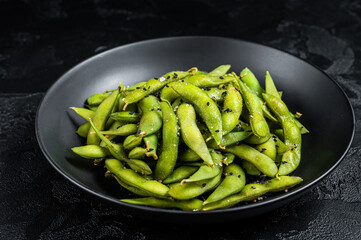 Boiled Edamame Soy Beans with sea salt in a plate. Black background. Top view