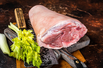 Fresh Raw pork shank knuckle on a butcher board with herbs for cooking. Dark background. Top view