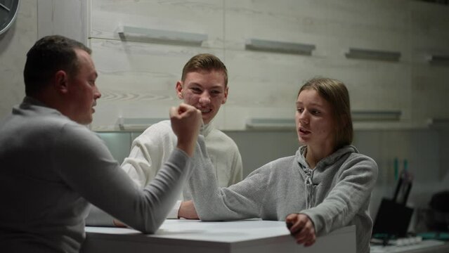 A father teaches teenagers arm wrestling in the kitchen