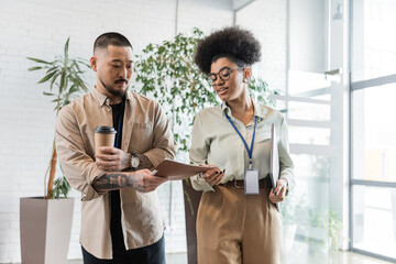 asian man showing folder with startup plan to african american businesswoman in office hall