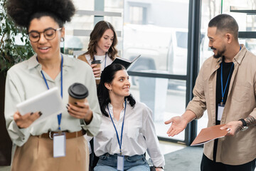 Fototapeta premium smiling asian man holding folder and discussing project with businesswoman near female colleagues