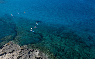 Fototapeta na wymiar Done view of unrecognized people kayaking in the sea. People active, healthy lifestyle. Cape Grego Cyprus