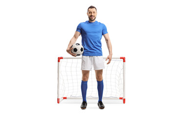 Full length portrait of a soccer player holding a ball in front of a mini goal