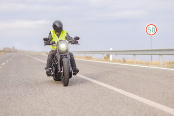 Man with a reflective safety vest riding a chopper motorbike on an open road
