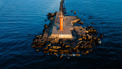 An orange lighthouse at the end of the Mangalsala or Eastern pier in Riga, Latvia where the river Daugava flows into the Baltic Sea.