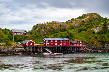 Wooden red house on the sea coast in Norway on Lofoten island with harbor and ships under the rock.