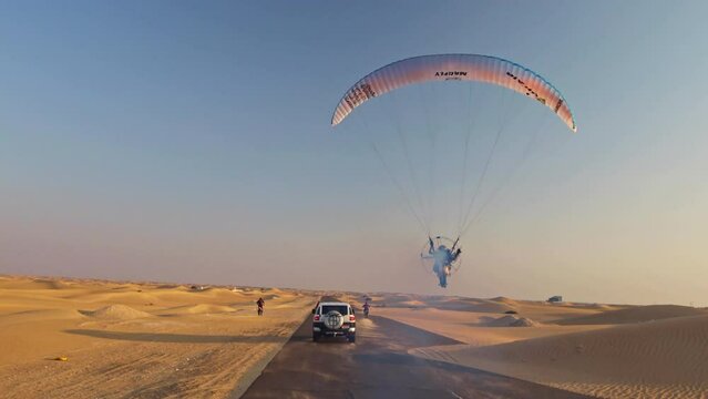 Epic shot of motorcyclists, car and paramotor speeding down the same desert road