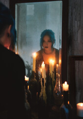 Indoors portrait of lovely goth girl among candles. Blue-haired gothic lady looking into old dirty...