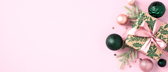 Christmas banner with vintage gift box, fir branches, green and pink baubles on pastel pink background. Top view with copy space.