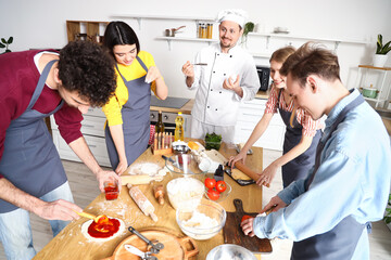 Group of young people with Italian chef preparing pizza during cooking class in kitchen