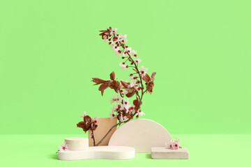 Decorative podiums and blooming branch on green background