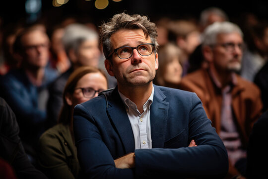 A Man Sitting In Front Of A Large Crowd Of People. This Image Can Be Used To Represent Leadership, Public Speaking, Or Being The Center Of Attention.