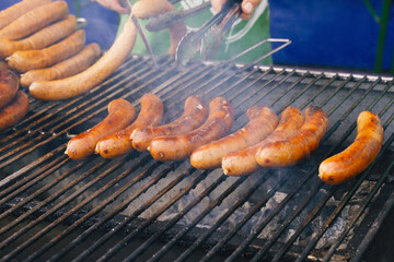 The cook prepares grilled sausages on a grill over coals.