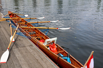 Ein Ruderboot, Mehrsitzer hat an einem Steg an einem Boothaus fest gemacht.