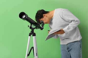 Young man with telescope and notebook on green background