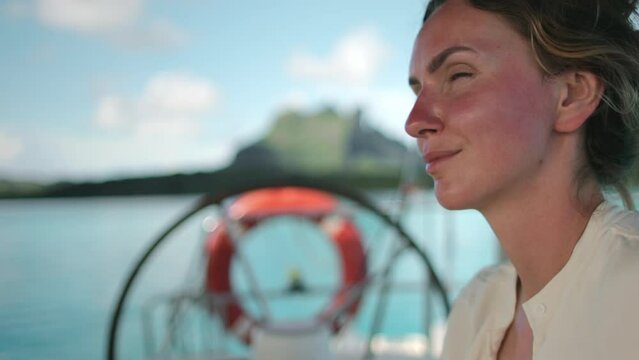 Tourist woman portrait enjoy cruise yacht trip to Bora Bora island, sailing at summer. Yacht ship helm rotates in background. Female relax outdoor lifestyle on sail yacht tropical travel vacation. 4K