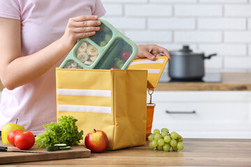 Woman packing fresh meal into lunch box bag in kitchen