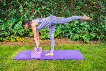 Fit woman in sportswear practices yoga pose using a block outdoors. Yoga with brick.