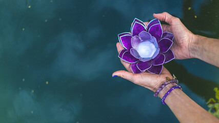 Top angle view of hands holding a purple glass lotus over water. Yoga and meditation concept. Copy space - obrazy, fototapety, plakaty