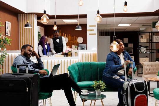 Tired People With Luggage Wait At Hotel Lobby, African American Man And Woman Tourists Wait To Check-in. Black Family Couple Arrived At Resort For Vacation, Resting After Long Flight