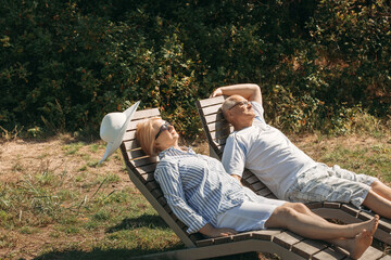 A couple of cute elderly people lie on sunbeds holding hands.