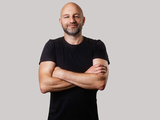 Bald man with beard in black t shirt on light color background. Man with athletic slim body. Sport...